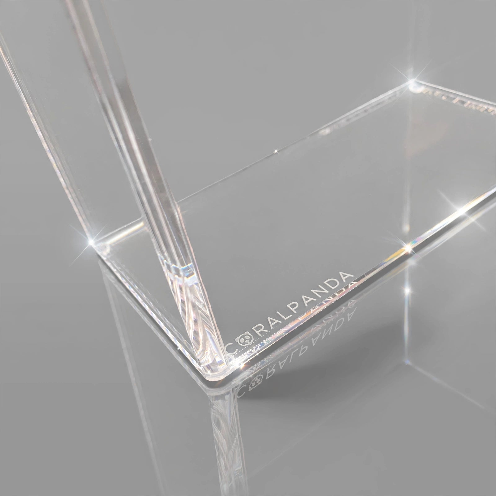 Clear acrylic rectangular display stand with corner brackets and a vertical support leg, featuring the brand name 'CORAL PANDA' printed on one edge, shown on a reflective gray surface.