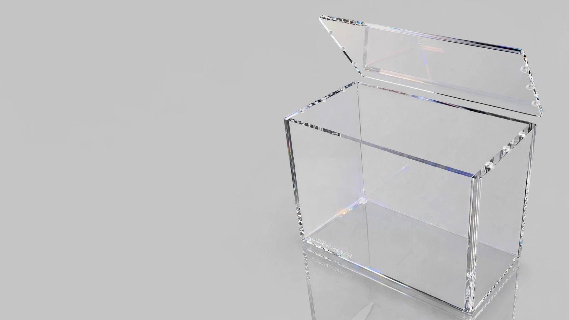 A clear acrylic or glass storage box with an open hinged lid, shown on a light gray reflective studio background.