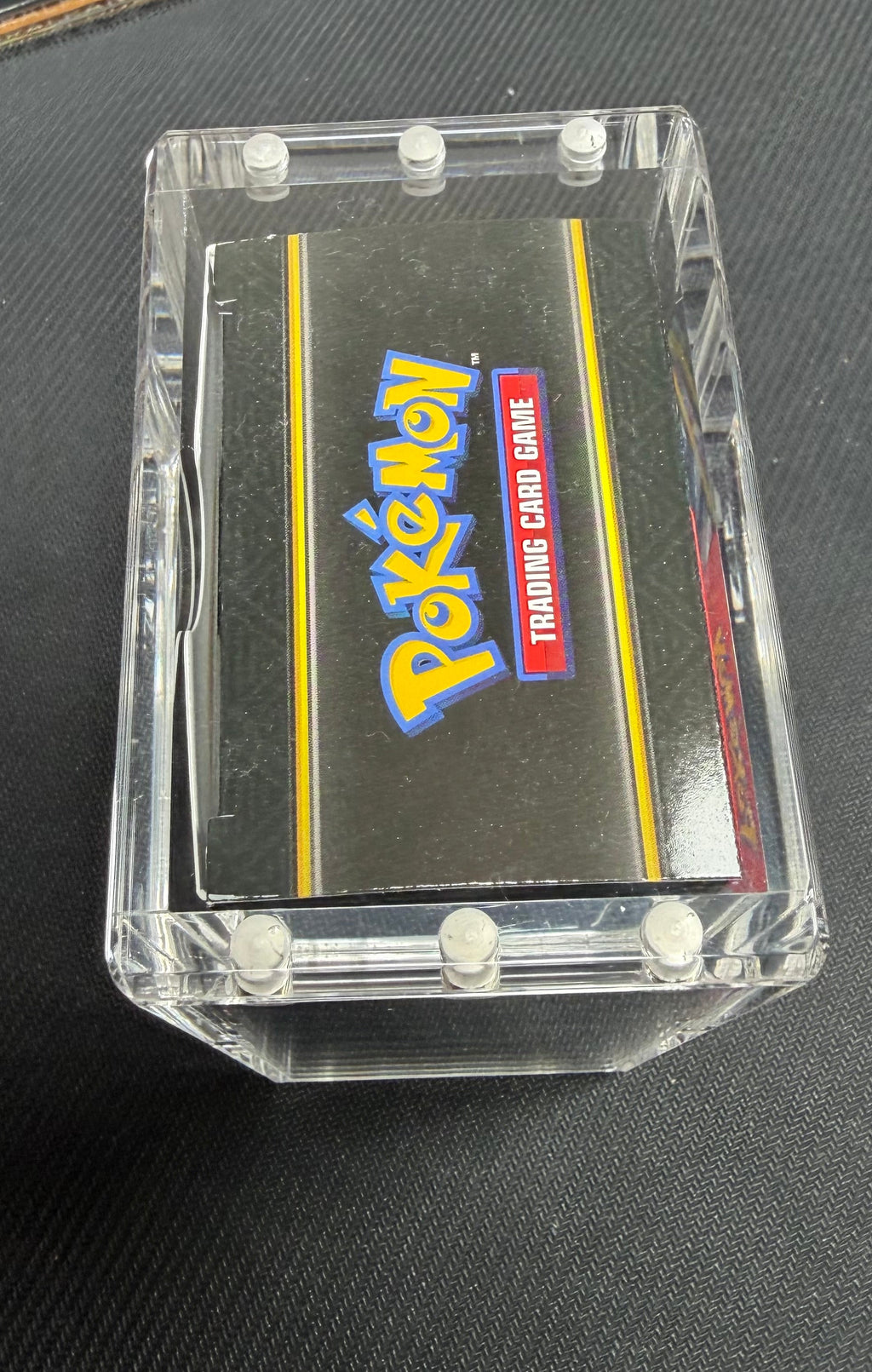 A Pokémon Trading Card Game cartridge in a clear plastic protective case, photographed on a dark textured surface.