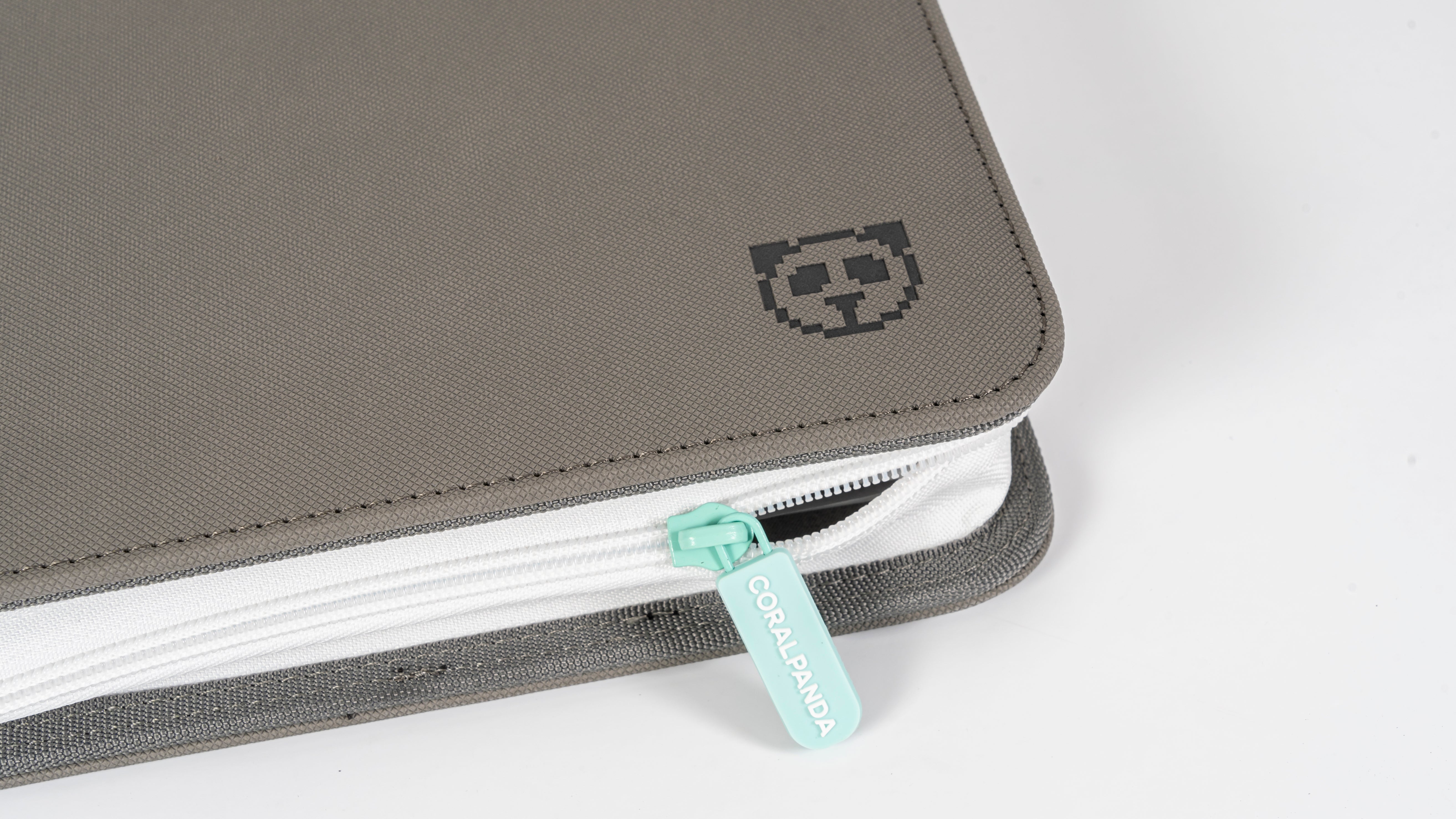A close-up of a gray fabric zippered pouch or sleeve with a white zipper track, a mint green pull tab, and a small pixel-style cat logo on the corner.